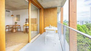 A balcony with a metal railing, a dining area with a table and chairs, and a view of the cityscape.