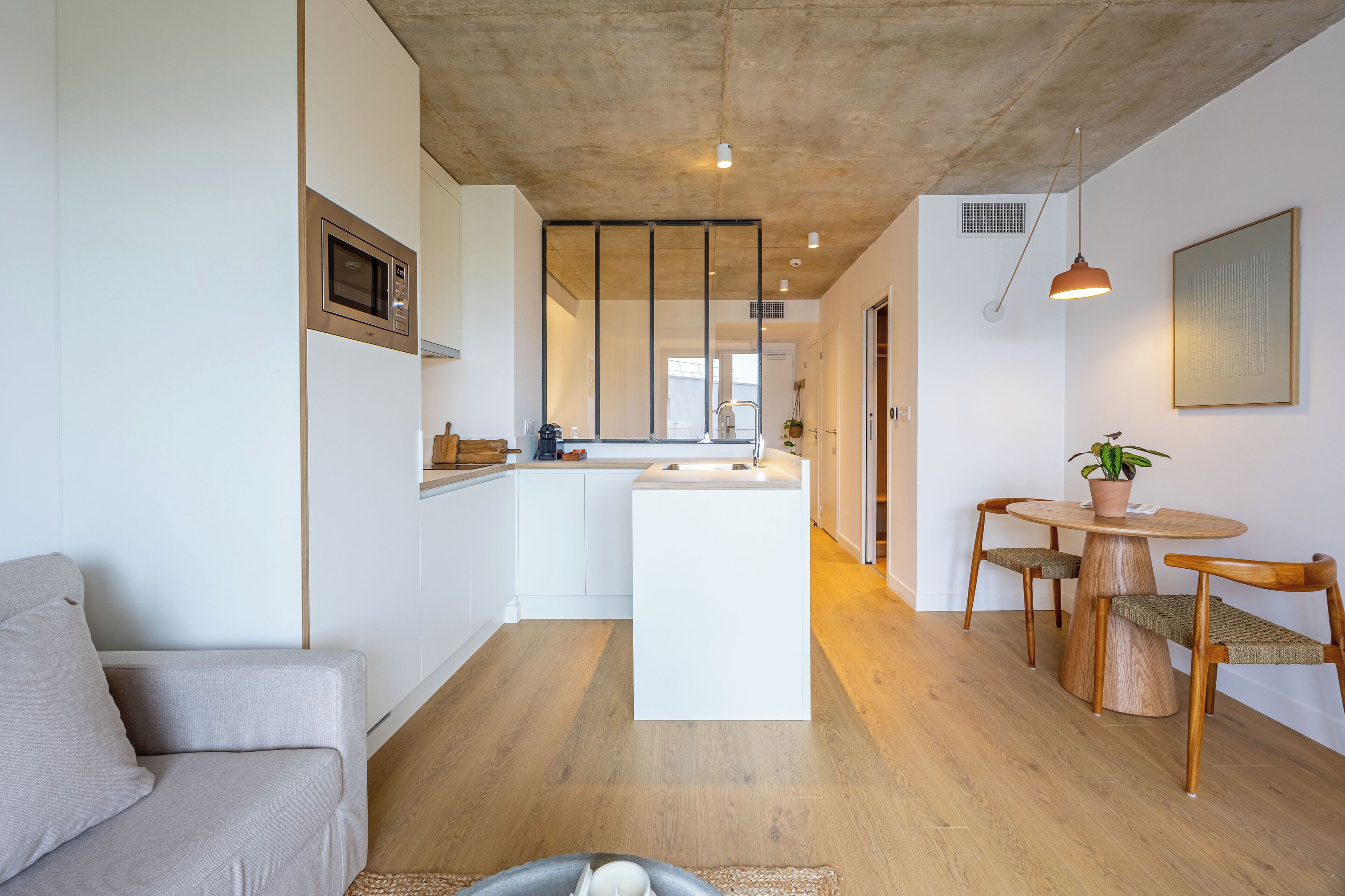 Cozinha moderna com ilha central, mesa de jantar de madeira com cadeiras e um sofá.