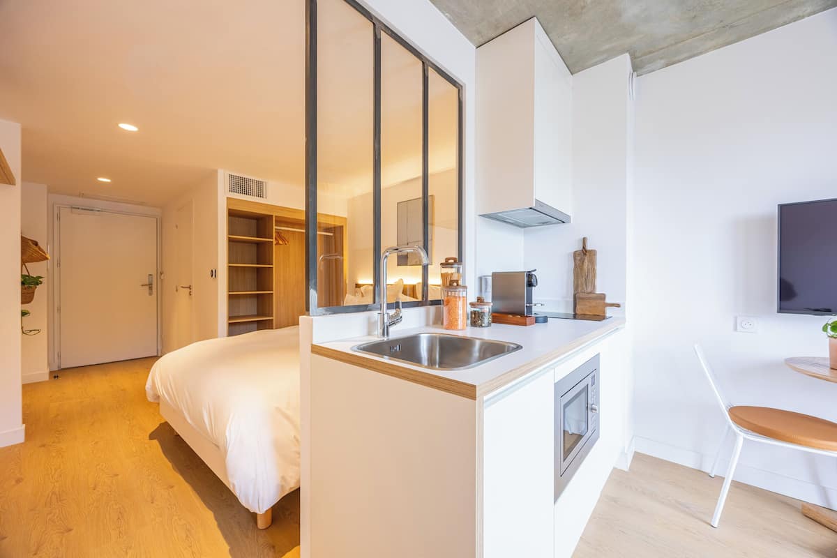Moderni hotellihuone, jossa on sänky, pieni keittiö, televisio ja kylpyhuone.