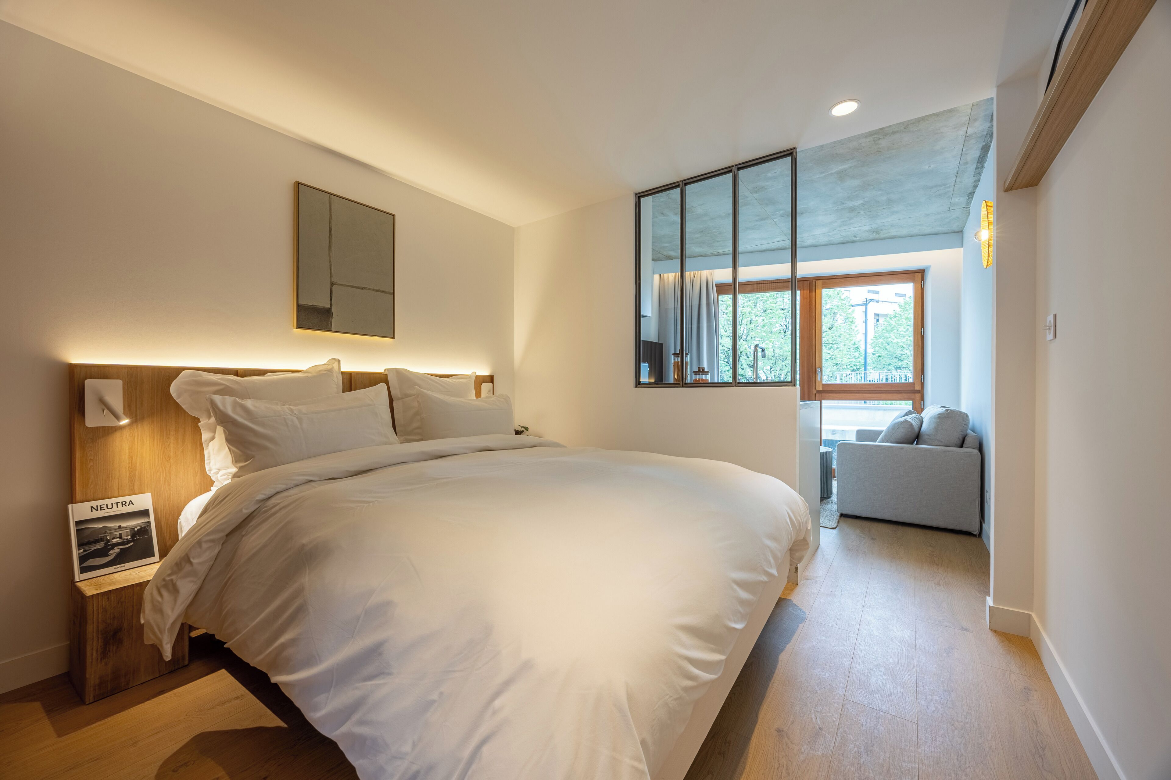 Un dormitorio moderno con una cama grande, una mesita de noche con lámpara, un espejo y vistas a un balcón.