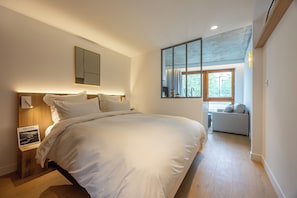 Un dormitorio moderno con una cama grande, una mesita de noche con lámpara, un espejo y vistas a un balcón.