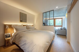 Un dormitorio moderno con una cama grande, una mesita de noche con lámpara, un espejo y vistas a un balcón.