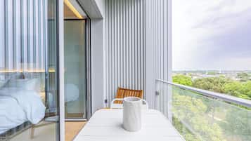 Un balcón con una mesa blanca, una silla de madera y un florero de mármol.