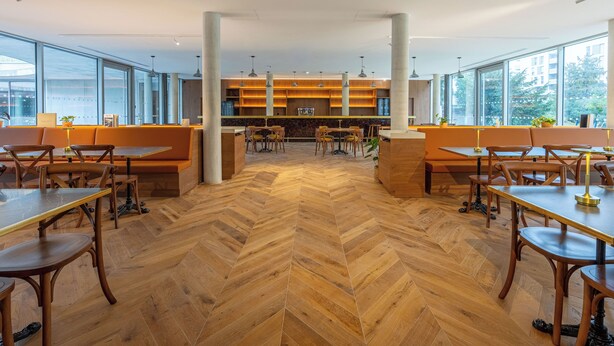 A modern dining area with wooden flooring, high ceilings, and large windows.