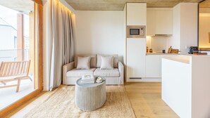 A modern living room with a sofa, a round coffee table, and a kitchen area with a microwave.