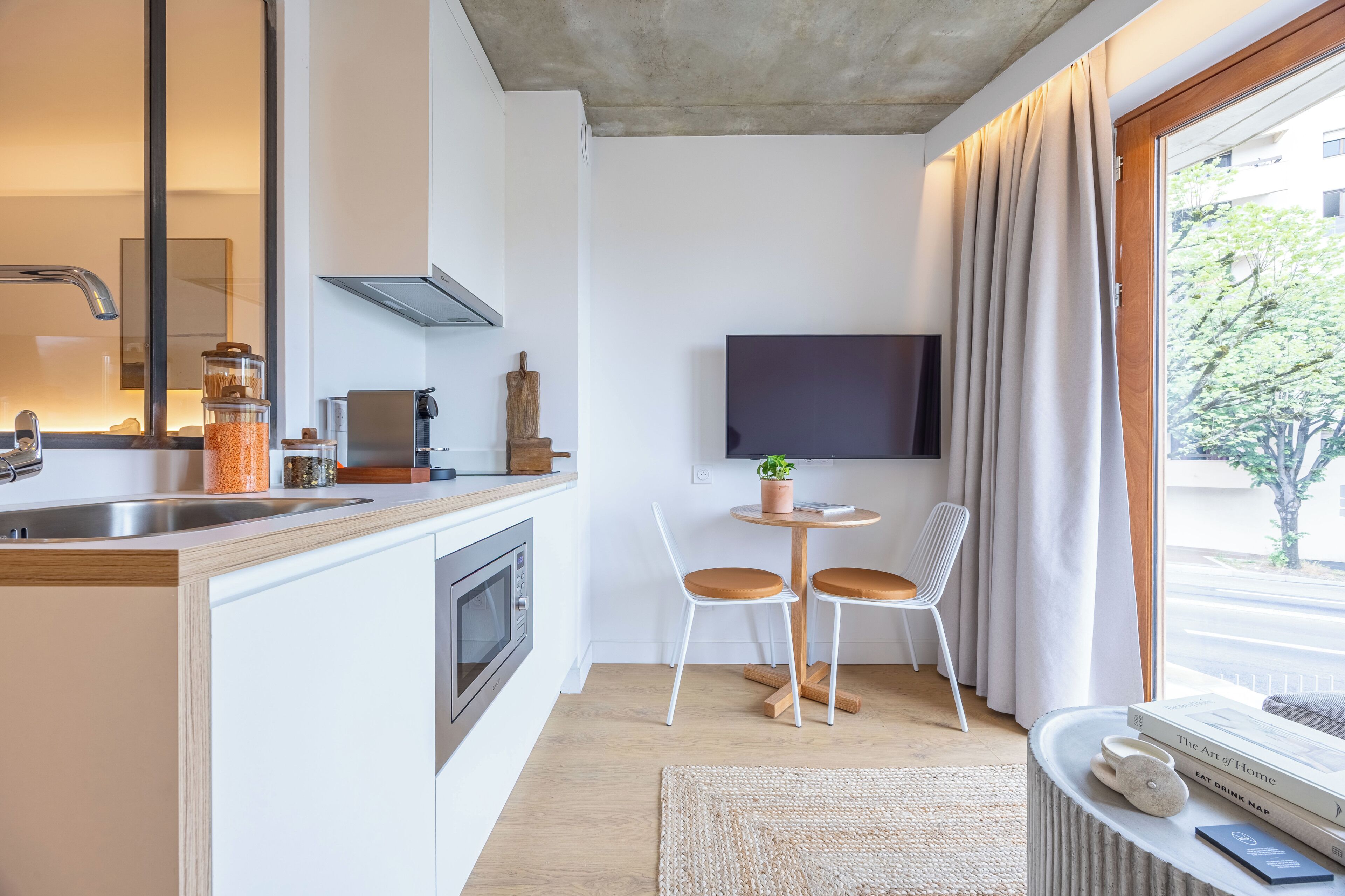 Una cocina moderna con horno empotrado, cafetera y comedor con dos sillas y una pequeña mesa.