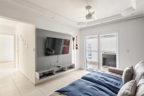 A modern living room with a flat-screen TV, a ceiling fan, and a sliding glass door leading to a balcony.