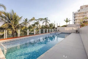 Una piscina con borde de azulejos, rodeada de palmeras y un edificio.
