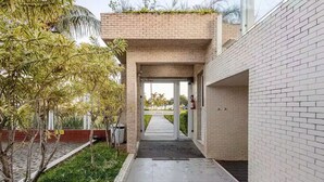 A covered walkway with a brick wall, a metal gate, and a pathway leading to a building entrance. - Beautiful beachfront apartment with unobstructed ocean views, pool, and sauna. (Bertioga)