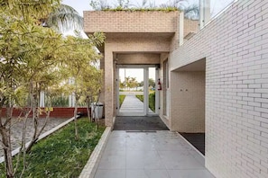 Un pasaje cubierto con un muro de ladrillo, una reja metálica y un camino que lleva a la entrada de un edificio.
