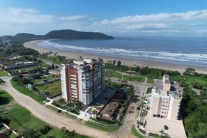 A coastal area with a beach, a large building with multiple floors, and a smaller adjacent building.