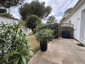 A paved courtyard with potted plants, a wooden gate, and a white building. - Charming house, pets welcome - 4 guests (Saint-Jean-de-Monts)