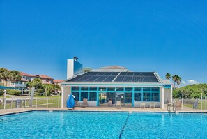 Ein Pool mit überdachtem Bereich, ein Gebäude mit großen Fenstern und ein klarer, blauer Himmel.