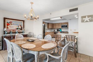 A dining area with a wooden table, white chairs, a chandelier, and a beach-themed wall art. - ⭐Enclave 203B ☀Walk to the Beach ☀Community Pool~Tennis and Volleyball Courts⭐ (Destin)