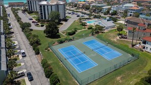 Zona residencial con dos canchas de tenis, un estacionamiento y vista al océano.