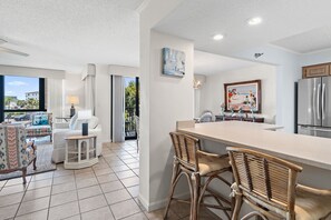 A modern kitchen with a large island, bar stools, and a dining area with a view. - ⭐Enclave 203B ☀Walk to the Beach ☀Community Pool~Tennis and Volleyball Courts⭐ (Destin)