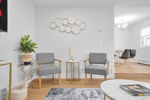 Un salón moderno con dos sillones grises, una mesita redonda, una planta en maceta y un adorno en la pared.