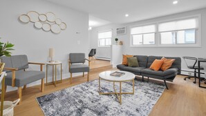 Ein modernes Wohnzimmer mit einem grauen Sofa, zwei Sesseln, einem Couchtisch und einem gemusterten Teppich.