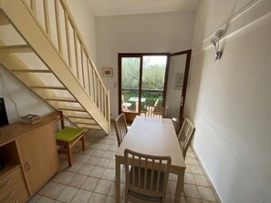 Ein Zimmer mit Esstisch, Stühlen, einer Treppe, einem TV-Schrank und Blick ins Freie.