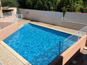 Ein rechteckiger Swimmingpool mit einem Metallzaun, umgeben von einer beigen Mauer und einem weißen Gitter.