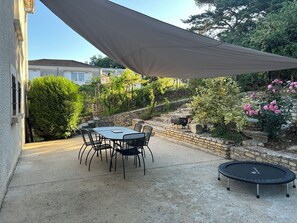 A patio with a table and chairs, a trampoline, and a stone wall with greenery. - Maison Cœur de Famille - Between town and country (Chauvigny)