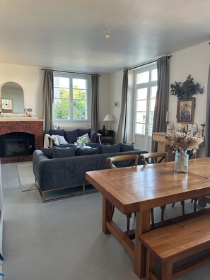 A living room with a fireplace, a sofa, a dining table, and a view of greenery outside. - Maison Cœur de Famille - Between town and country (Chauvigny)