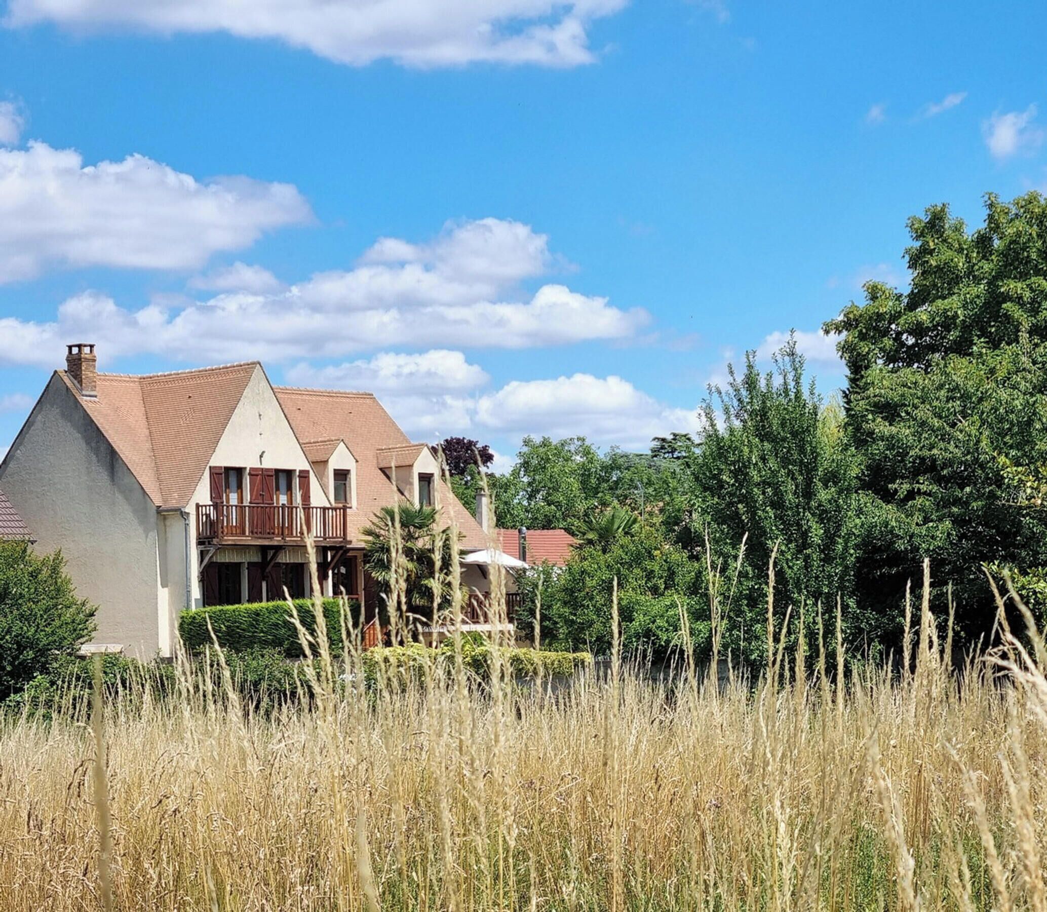 Een huis met twee verdiepingen, met een rood dak, omringd door hoog gras en bomen.