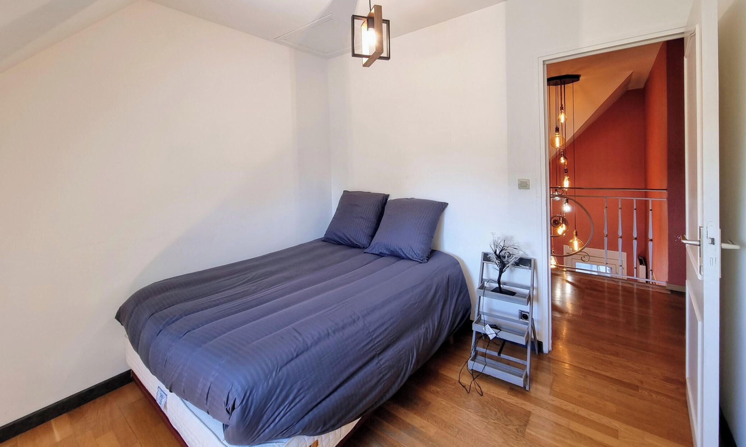A bedroom with a bed, a nightstand, and a staircase leading to an upper level.