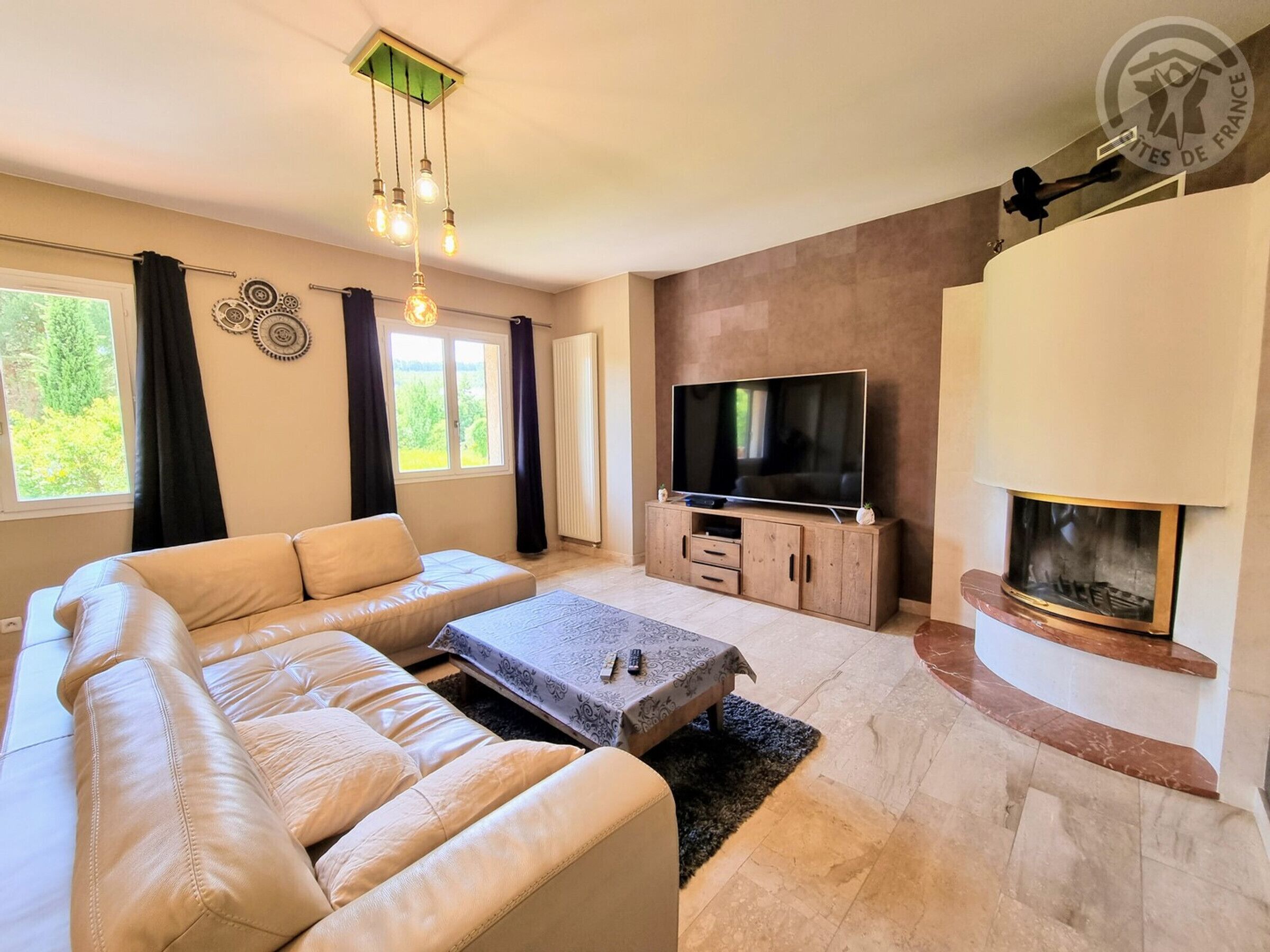 Un salon moderne avec un canapé d’angle, un téléviseur à écran plat, une cheminée et un luminaire au plafond.