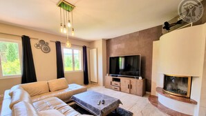 A modern living room with a sectional sofa, a flat-screen TV, a fireplace, and a ceiling light fixture.