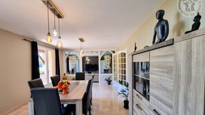 A modern dining area with a wooden table, black chairs, pendant lights, and a cabinet with glass doors.