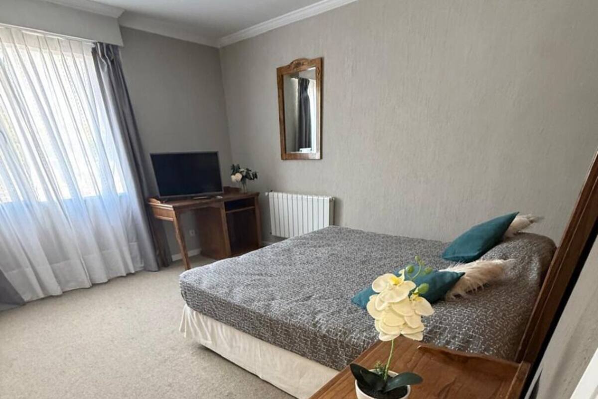 A bedroom with a bed, a desk, a television, a mirror, and a window with curtains.