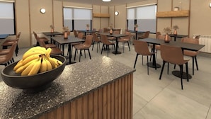Un comedor moderno con varias mesas y sillas, una barra central con un tazón de plátanos e iluminación colgante.
