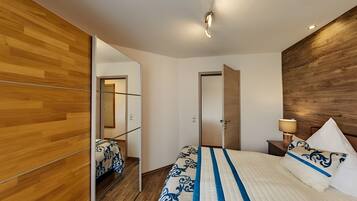 A modern bedroom with a wooden floor, a bed with a patterned bedspread, a bedside lamp, and a mirror.