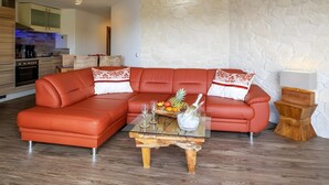 A modern living room with a sectional sofa, a glass coffee table, and a stone wall. - Exclusive Apartment for 4 People (56 m²) in Schalkenmehren with Lake View (Schalkenmehren)