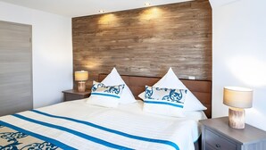 A neatly made bed with a striped bedspread, two decorative pillows, a wooden headboard, bedside lamps, and a nightstand. - Exclusive Apartment for 4 People (56 m²) in Schalkenmehren with Lake View (Schalkenmehren)