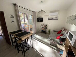 Ein Wohnzimmer mit einer Couch, einem Fernseher, einem Tisch mit Stühlen und einer Glastür zu einem Außenbereich.