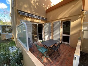Eine Terrasse mit Tisch, Stühlen, einer Glasgleittür und einem kleinen Garten.