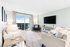 Et hotelværelse med balkon, sofa, fjernsyn og et bord med lampe.