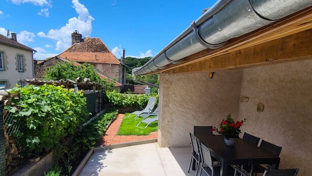 A patio with a table and chairs, a potted plant, and a view of a garden and buildings. - Spacious house - 6 guests (Tignécourt)