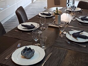 Une table à manger dressée avec des assiettes, des couverts, des verres et des serviettes.