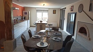 A dining area with a table set for four, a kitchen in the background, and a fireplace. - Spacious house - 6 guests (Tignécourt)