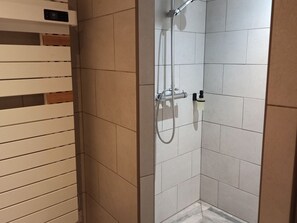 Une douche équipée d’un pommeau de douche à main et d’un robinet mural, avec des murs carrelés et un panneau en bois sur le côté gauche.