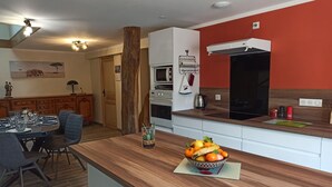 A modern kitchen with a wooden countertop, a fruit bowl, and a dining area with a table set for four. - Spacious house - 6 guests (Tignécourt)