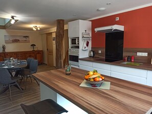 Une cuisine moderne avec un plan de travail en bois, un panier de fruits et un coin repas avec une table dressée pour quatre personnes.