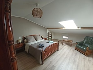 A bedroom with a wooden bed, a green leather chair, a small table, a ladder, and a skylight.