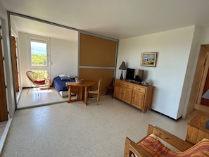 A room with a bed, a TV, a wooden cabinet, a chair, a table, and a sliding door leading to a balcony. - Apartment 4 guests with sea view (Argelès-sur-Mer)