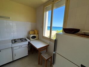 A compact kitchen with a gas stove, microwave, and refrigerator, a wooden chair, and a window with a beach view. - Apartment 4 guests with sea view (Argelès-sur-Mer)