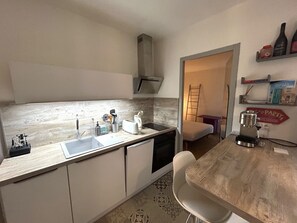 A compact kitchen with a sink, a toaster, and a coffee maker. There is a chair and a small table.