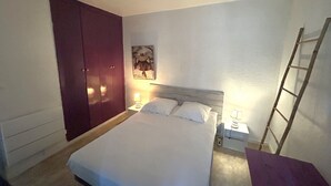 Une chambre à coucher avec un lit, une armoire, une table de chevet, une lampe, un tableau au mur et une échelle.